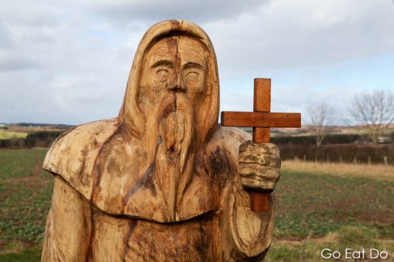 Carved wooden statue of Saint Cuthbert holding a crucifix on St