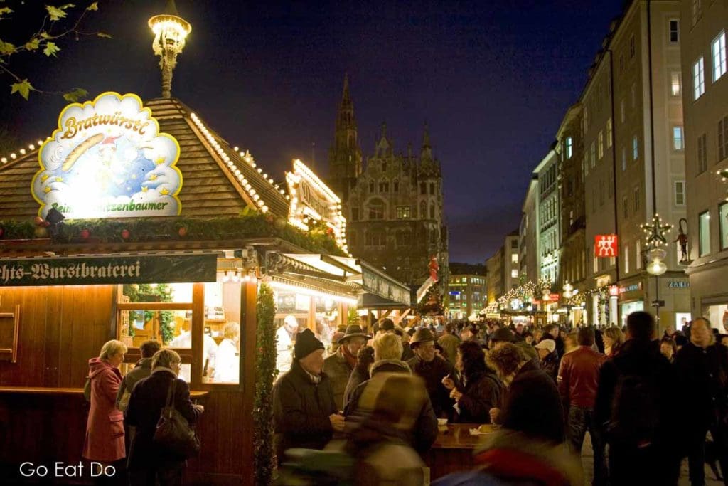 People meet over warm drinks and traditional seasonal food by stalls at a Munich Christmas market, the Christkindlmarkt behind the Neues Rathaus (New Town Hall).