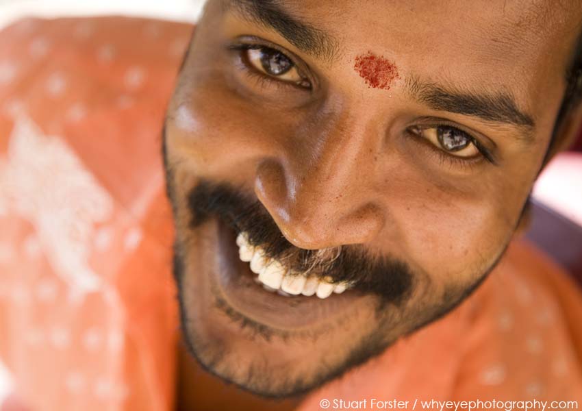 A smiling Indian rickshaw driver with a tikka marking on his forehead in the city of Chennai, India