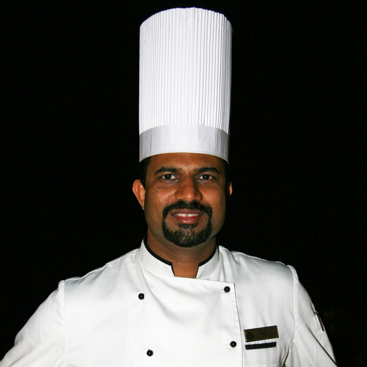 Chef Vijay Bakshi wearing a double-breasted white jacket and traditional toque blanche chef's hat