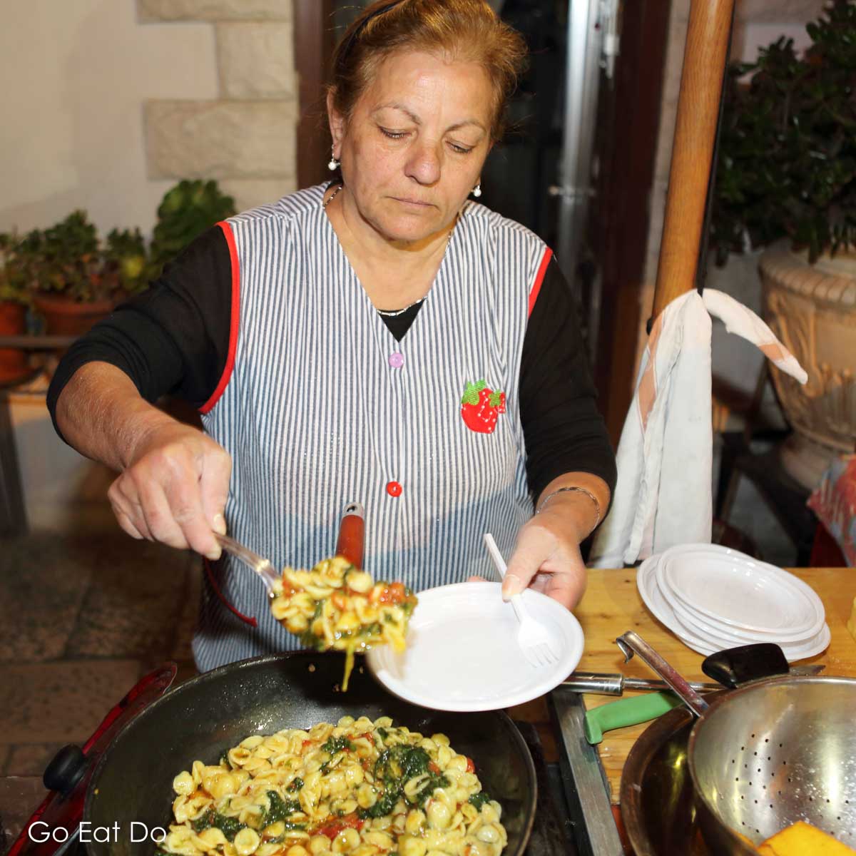 Carmela, a local woman, serves orecchiette, a local pasta dish, at an outdoor kitchen during a food tour of Bari.