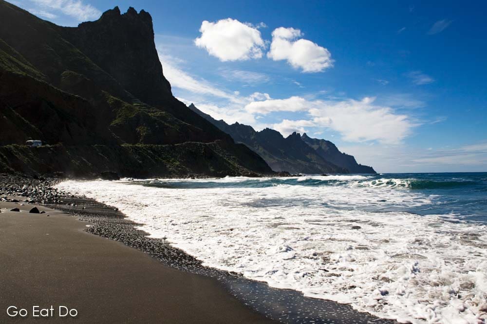 The Atlantic Ocean laps against black sand on Taganana Beach under cliffs near Santa Cruz de Tenerife