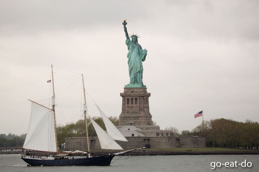 A clipper sailing ship sails past the Statue of Liberty on Liberty Island in New York City, USA