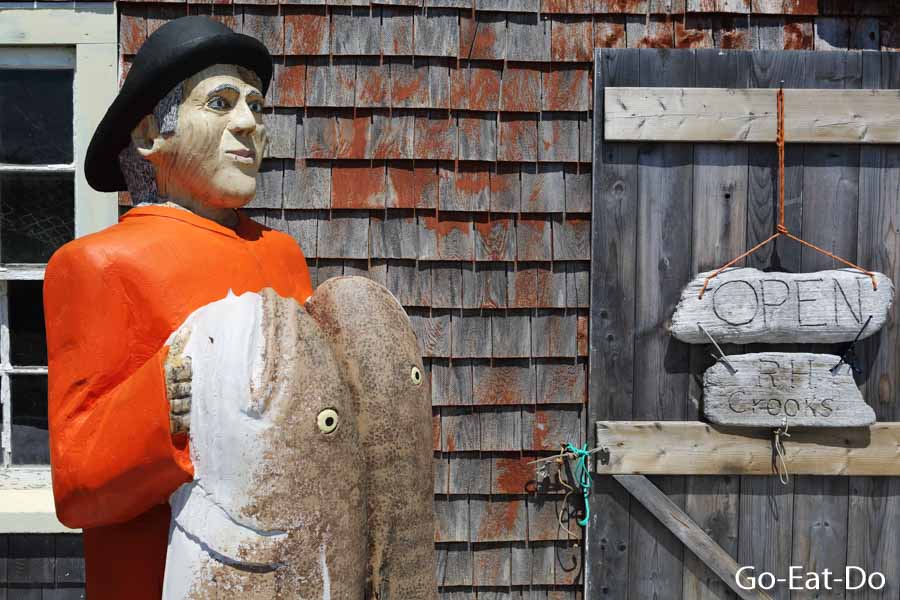 Fisherman figure holding fish outside of a rustic fishing hut at Peggy's Cove in Nova Scotia, Canada