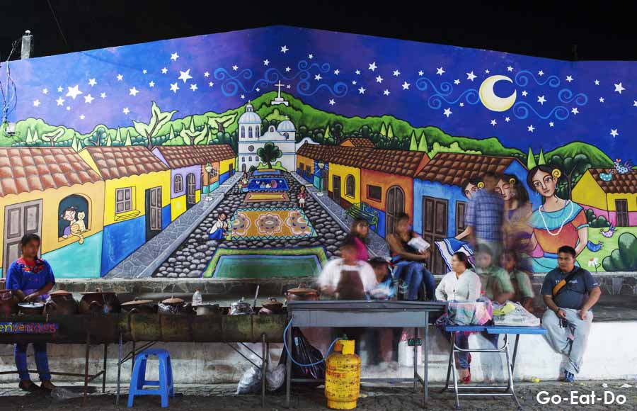 People sit by a colourful mural at night in Suchitoto, El Salvador