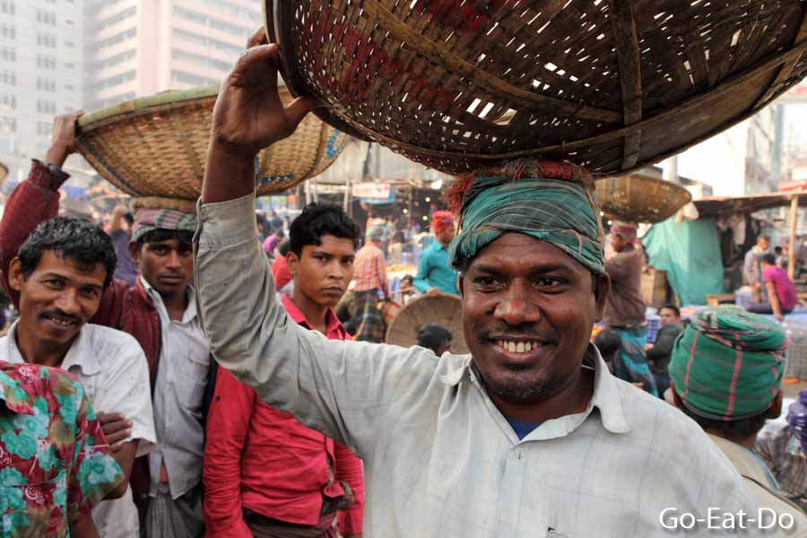 Smiling porter carries a basket on his head at Gulshan Market, where fruit and vegetables are sold, in Dhaka, Bangladesh