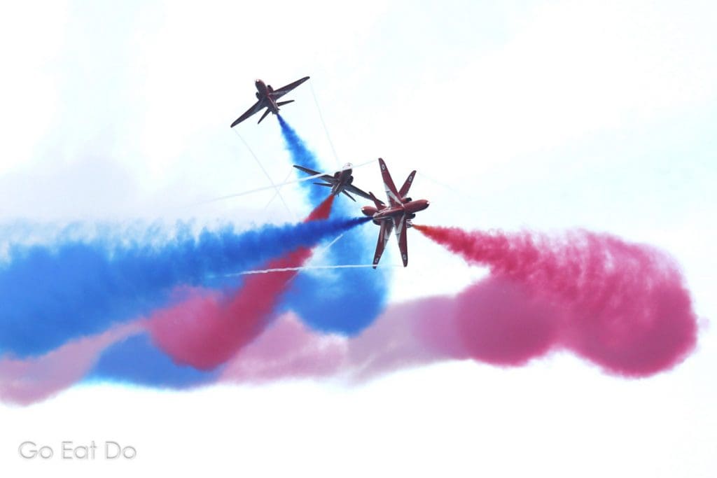 The Royal Air Force Red Arrows in close formation trailing colorful vapour.