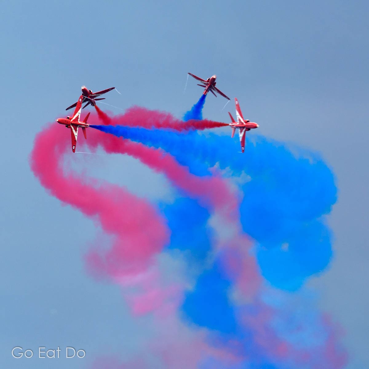 The Red Arrows trailing blue and red vapour as they break formation.