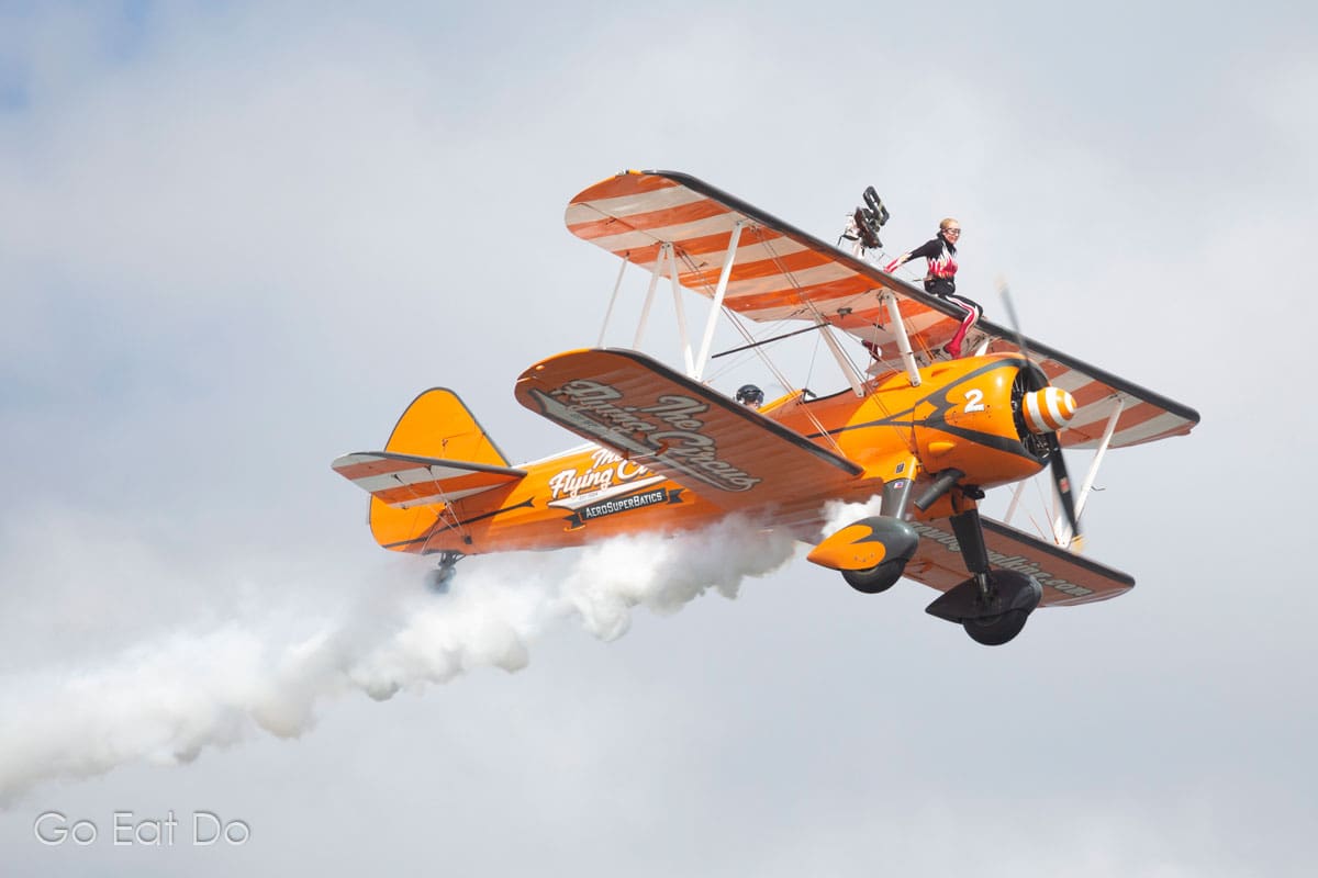 A woman sits on the upper wing of a biplane during a wingwalking demonstration during a summer air show.