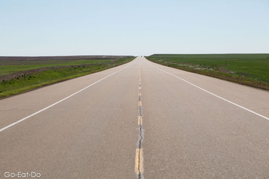 Long straight road on highway cutting through prairie land cultivated to grow grain in Alberta, Canada