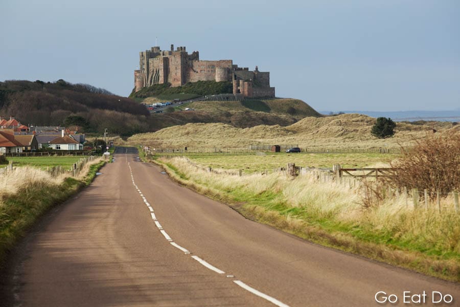 Bamburgh Castle, a medievel fortress, overlooks the Northumberland Coastal Route, a scenic driving route along the coast road in Northumberland, England