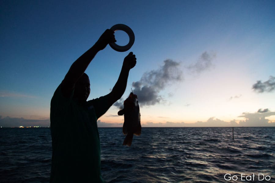 Silhouette of a man holding a fish caught while night fishing on the Indian Ocean off the Maldives