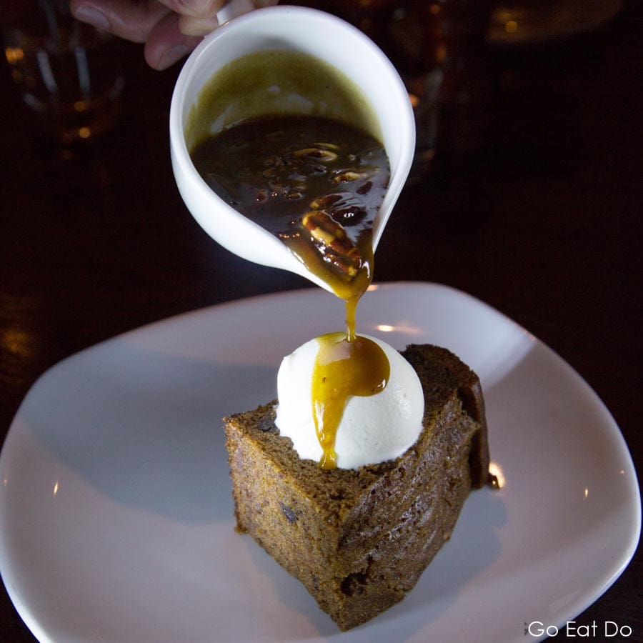 Traditional British dessert of sticky toffee pudding served with ice cream and a jug of toffee sauce served at The Rib Room at Ramside Hall restaurant in Durham, England