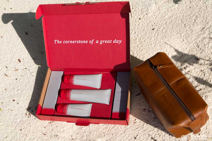 Box of Cornerstone shaving products and a leather travel bag on the white sand of a beach in the Maldives
