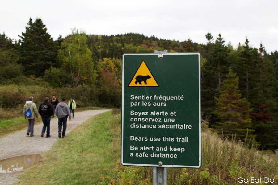 People walking by a sign warning that bears use the trail at Forillon National Park in Quebec, Canada