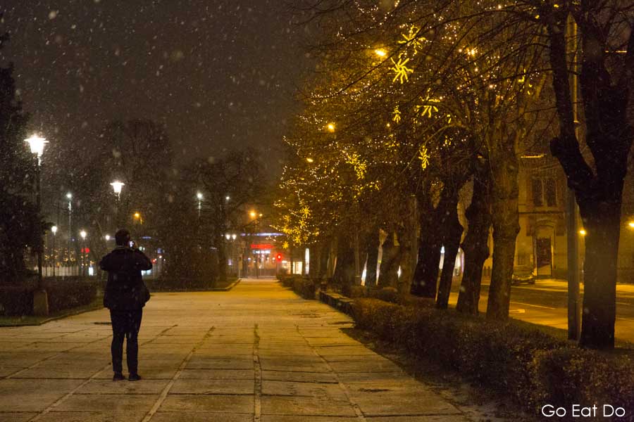 Woman photographs the street as snow falls at night in Riga, Latvia