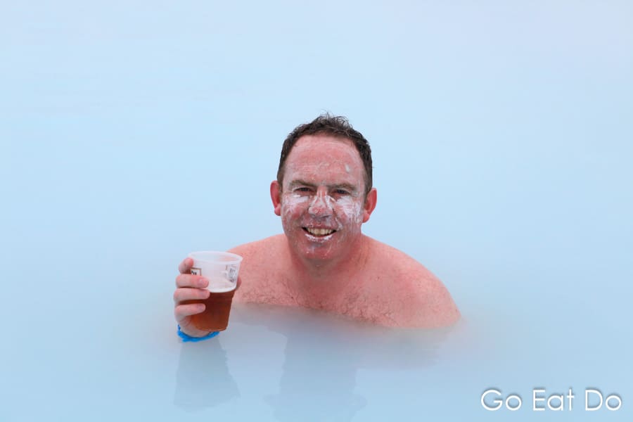 Travel blogger Stuart Forster holds a cold beer while mud is smeared on his face in the heated pool of the Blue Lagoon in Iceland