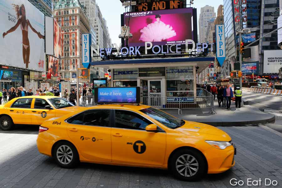 A yellow cab at Times Square driving in New York City. Experience a road trip in upstate New York to see more of the Big Apple state.