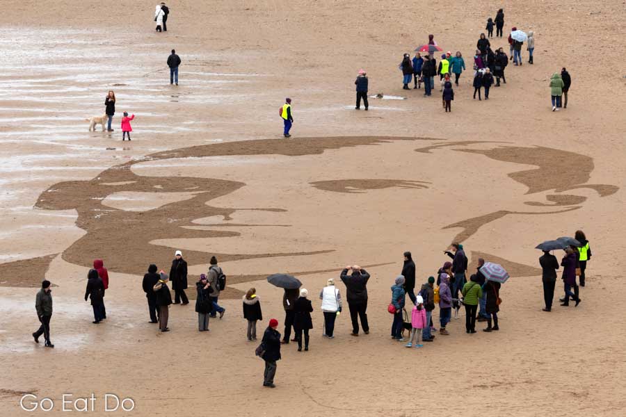 People standing on Roker Beach view a portrait of Hugh Carr, during Danny Boyle's Pages of the Sea in Sunderland, an event to commemorate 100 years since Armistice Day that marked the end of the war.