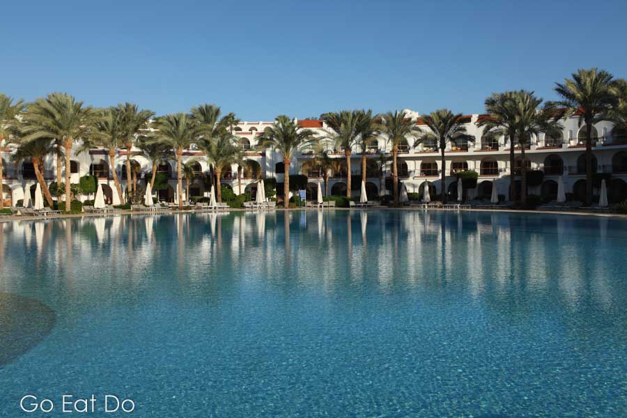 Rooms with verandas overlook a palm fringed swimming pool within the Royal Savoy Resort.