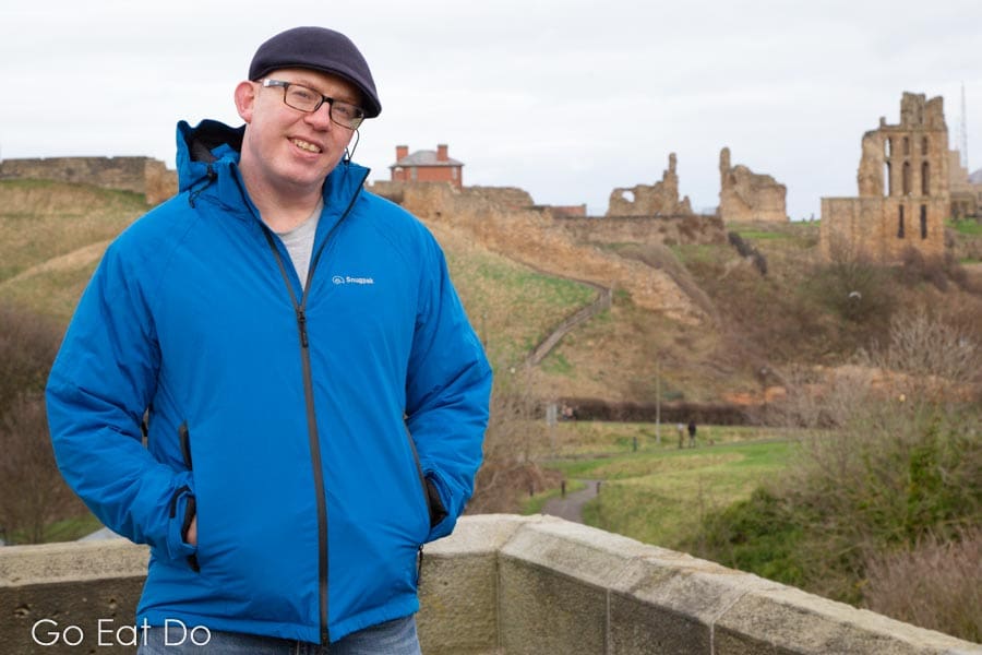 Stuart Forster wearing a blue Snugpak Torrent Jacket at Tynemouth Priory and Castle