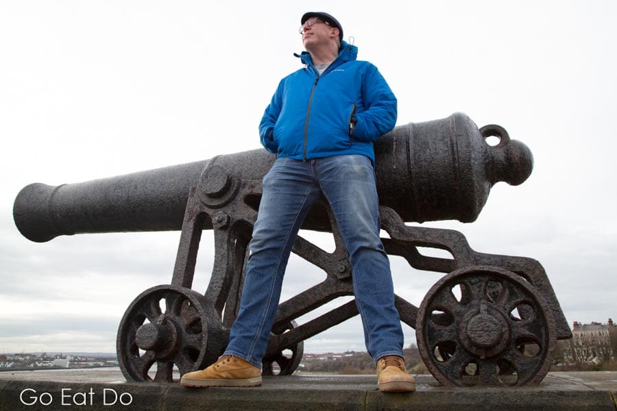 Travel blogger Stuart Forster wearing a Snugpak Torrent Jacket by one of the guns of the HMS Royal Sovereign from the Battle of Trafalgar