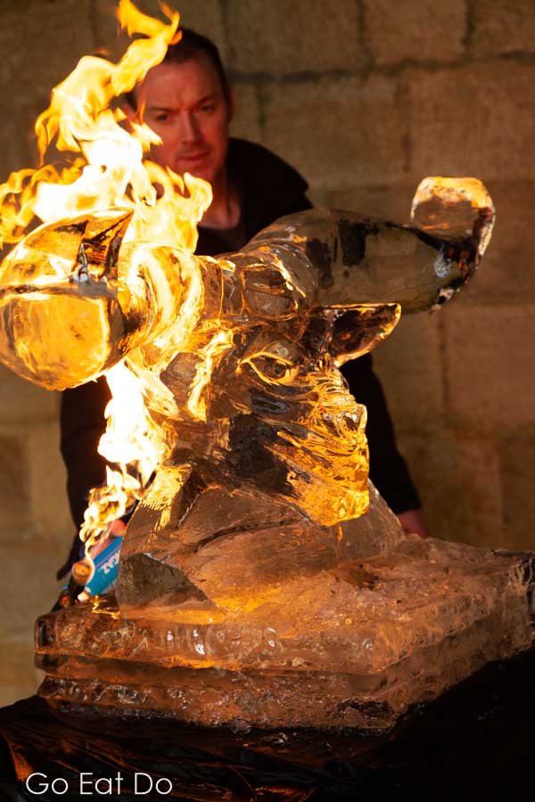 Sculptor Matt Chaloner looking at a flaming Minotaur sculpture displayed in the cloisters of Durham Cathedral