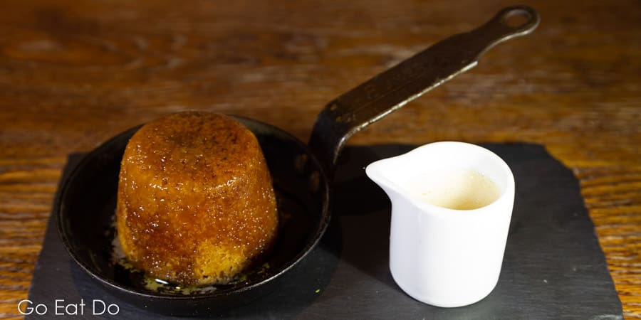 Sticky toffee pudding with caramel sauce served in a metal pan with a jug of custard at The Hope and Anchor in South Ferriby, Lincolnshire