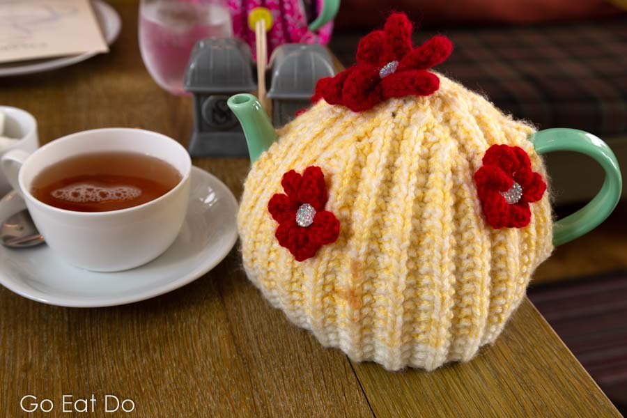 Cup of Earl Grey tea next to a teapot covered by a yellow knitted tea cosy at St Mary's Inn, Northumberland