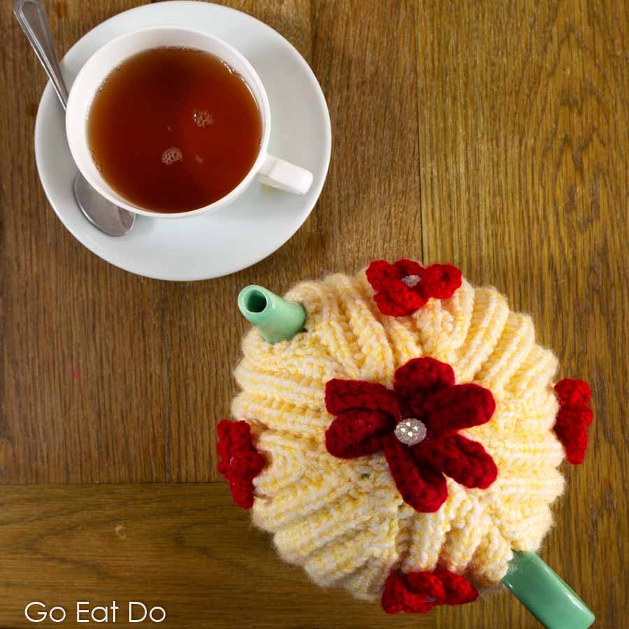 Cup of Earl Grey tea by a tea pot with a colourful knitted tea cosy served during a Northumberland afternoon tea.