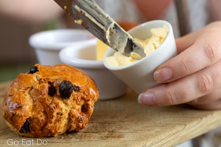 Woman puts clotted cream on a fruit scone during afternoon tea at St Mary's Inn, Northumberland