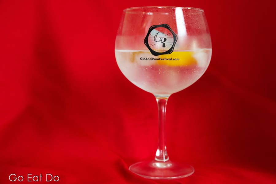 Gin and tonic served with ice and lemon in a copa glass against a red background