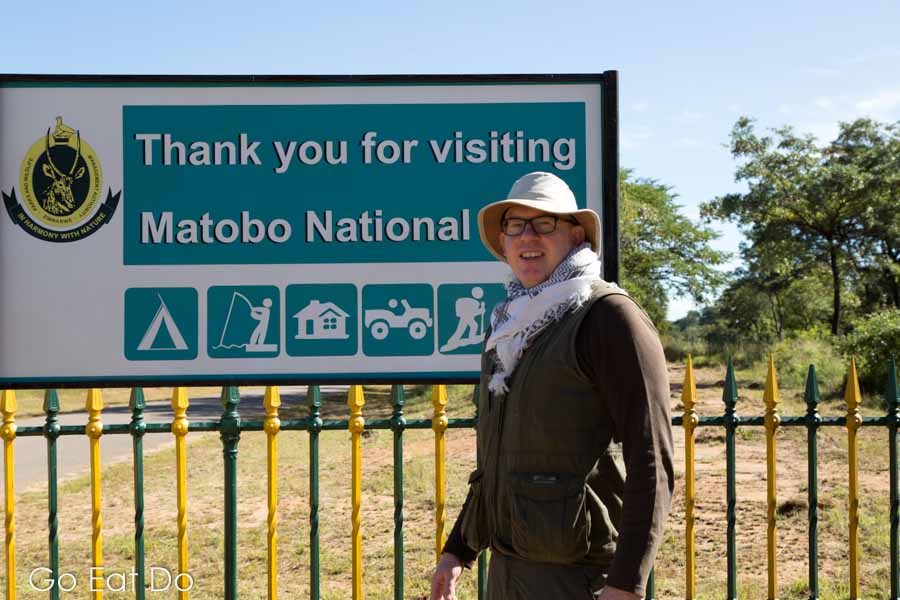 Travel writer Stuart Forster wearing a broad-brimmed hat by a sign for Matobo National Park, Zimbabwe