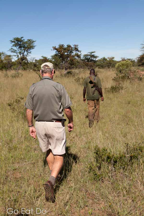 Guide walking behind a guard carrying an AK-47 assault rifle in Matobo National Park, Zimbabwe