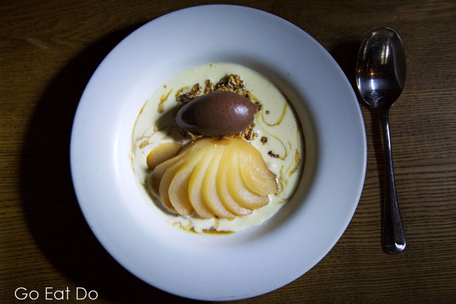 Dessert featuring poached pear and hazelnut ice cream. The dish is served with a creamy sauce.
