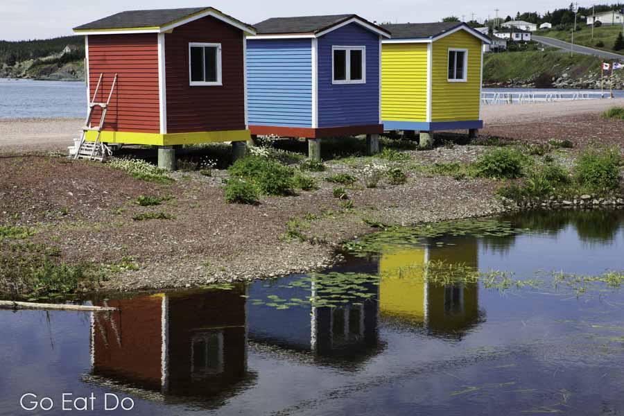 Colourfully painted huts by the shore of the Atlantic Ocean reflect in a pond at Heart's Delight-Islington in Newfoundland and Labrador.