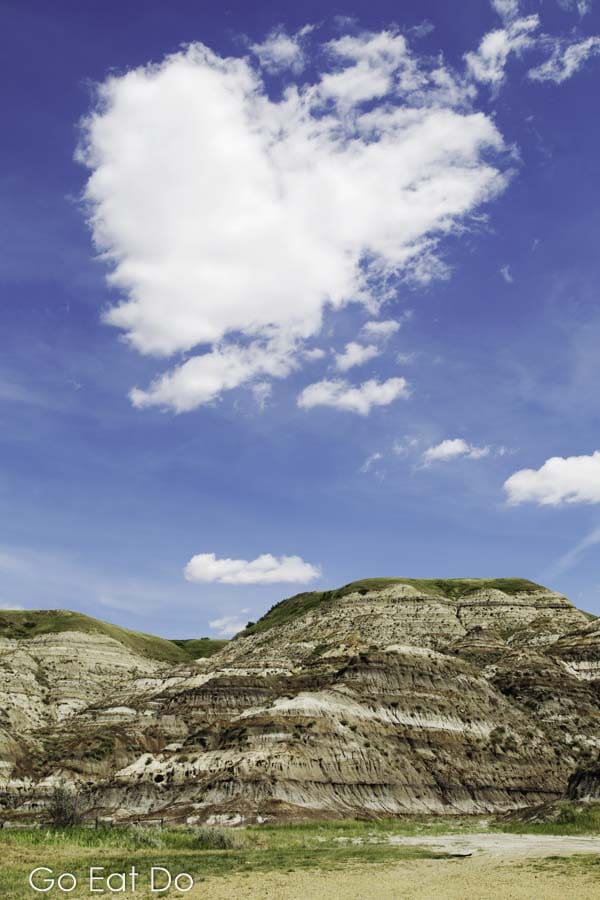 Heart-shaped cloud in blue sky above stratified rock in the Badlands of Alberta near Drumheller, Canada