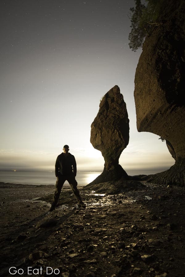 Travel blogger Stuart Forster standing at night by one of the Hopewell Rocks by the shore of the Bay of Fundy in New Brunswick, Canada