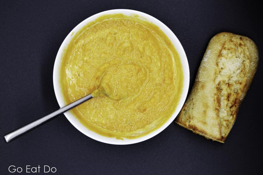 A freshly baked half of baguette next to a bowl of easy-to-make lightly spiced butternut squash soup