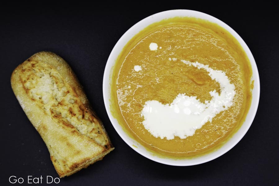 Freshly baked bread next to a bowl of lightly spiced butternut squash soup with an inelegant swirl of double cream