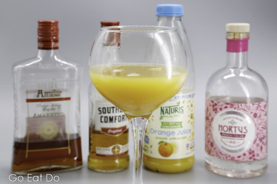 Glass of Alabama Slammer with the four ingredients used to mix the classic cocktail recipe