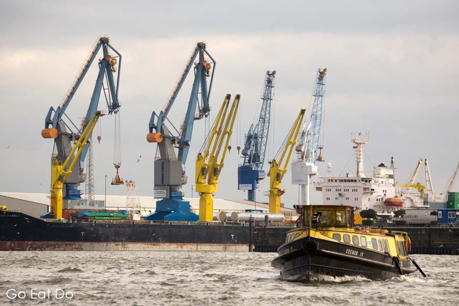 A boat on the River Elbe, in front of cranes in the Port of Hamburg, Germany