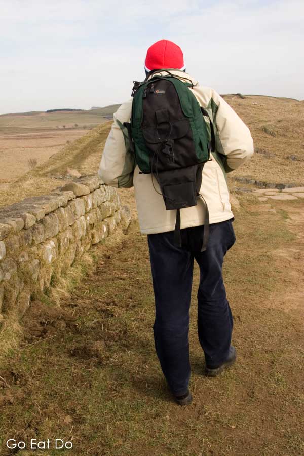 Man with a backpack walking Hadrian's Wall, a UNESCO World Heritage Site, in Northumberland National Park in northeast England
