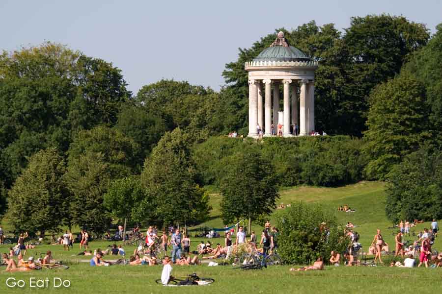 People enjoying a sunny day on a meadow below the Monopteros in the Englischer Garten in Munich, Germany