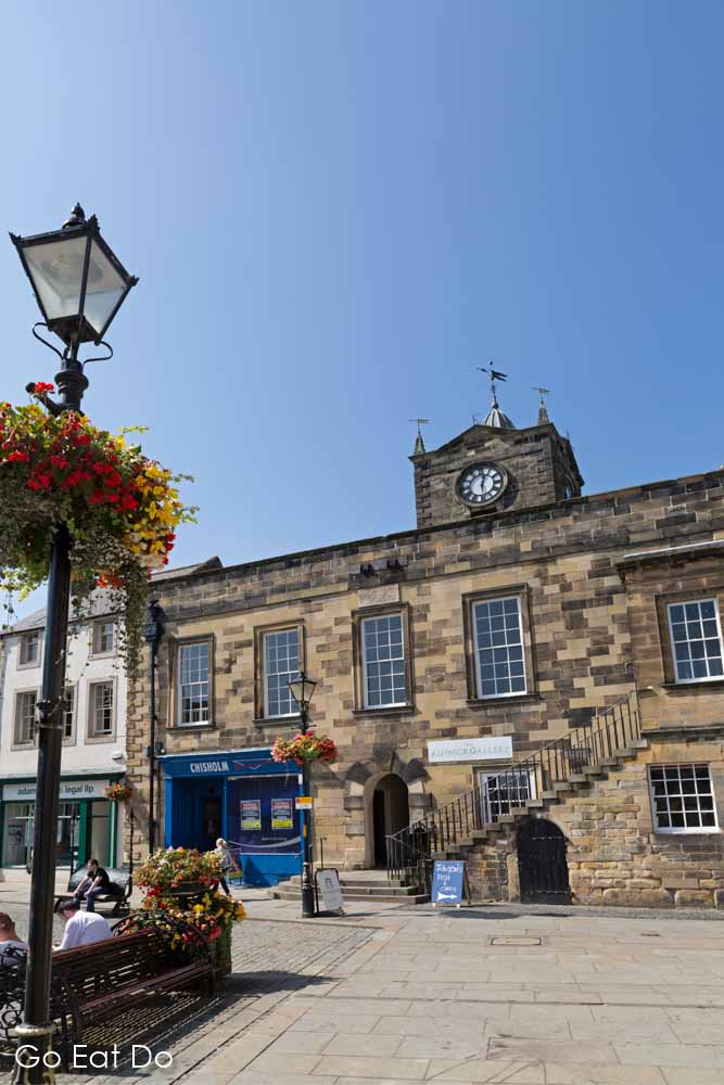 Hanging baskets on a streetlamp outside of the Old Town Hall, which hosts the Alnwick Gallery, at Alnwick in Northumberland, England