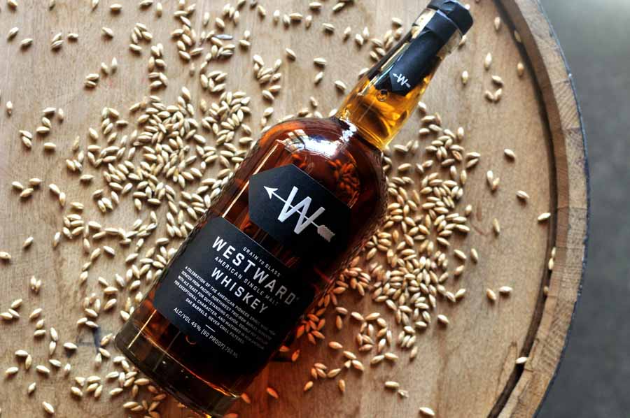 Bottle of Westward Single American Malt whiskey with barley on a wooden barrel