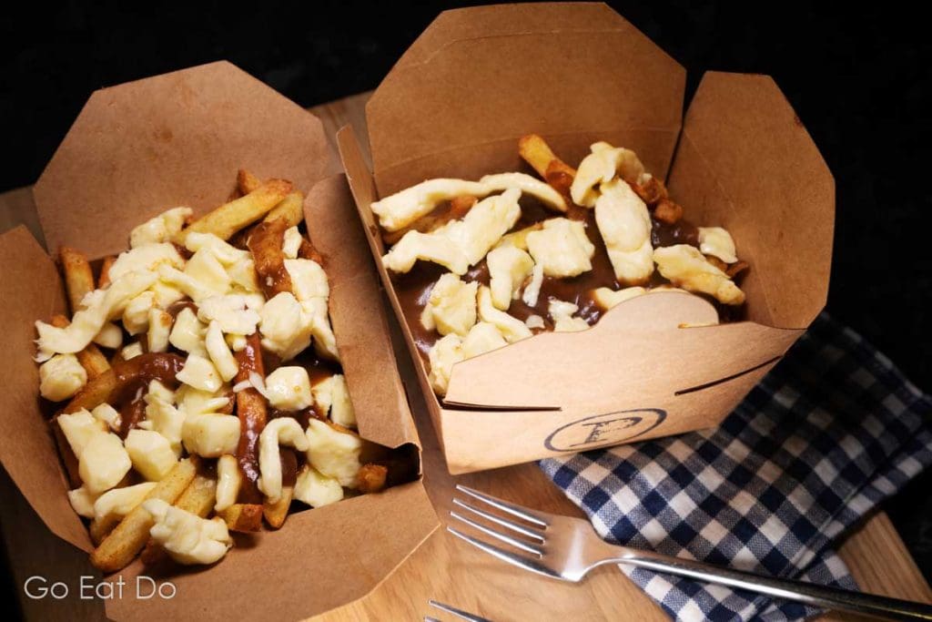 Two boxes of poutine made at home in boxes from The Poutinerie.
