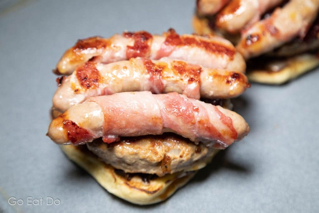 Pigs in blankets (bacon rashers on chipolata sausages) on top of a homemade turkey burger.