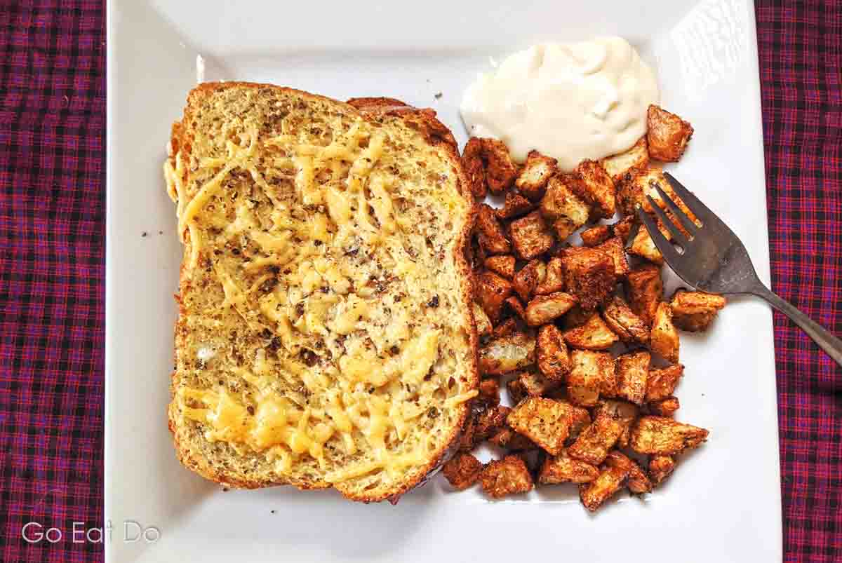 Oven-baked sandwich topped with melted, grated cheese with herb-crusted fried potatoes.