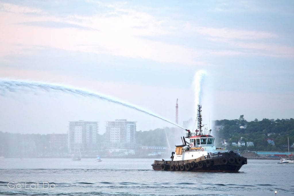 The Atlantic Oak tug boat shoots hoses into the air during the parade of sail as the Queen Mary 2 departs Halifax.